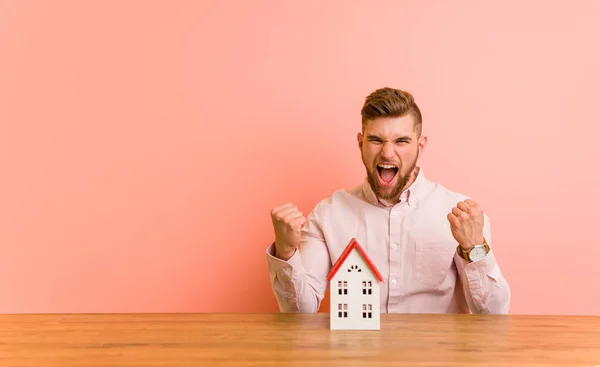 Young Caucasian Man Sitting House Icon Cheering Carefree Excited Victory — Stock Photo, Image