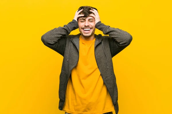 Young hispanic casual man laughs joyfully keeping hands on head. Happiness concept.