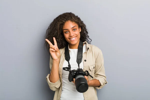 若いアフリカ系アメリカ人の写真家の女性が勝利のサインを示すカメラを持ち — ストック写真