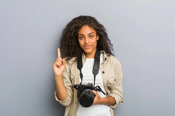 若いアフリカ系アメリカ人の写真家の女性は 指でナンバーワンを示すカメラを持って — ストック写真