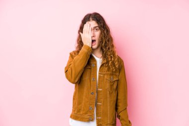 Genç, uzun saçlı adam yalnız poz veriyor. Yüzünün yarısını avuç içiyle kaplayarak eğleniyor..