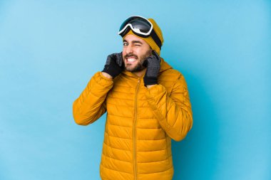 Genç kayakçı beyaz adam kulaklarını elleriyle kapatıyor..