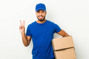 Genç Güney Asyalı kurye neşeli ve kaygısız parmakları olan bir barış sembolü gösteriyor..