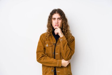 Uzun saçlı adam yalnız poz veriyor gülümsüyor ve kendinden emin, elleriyle çeneye dokunuyor..