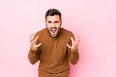 Pembe arka planda genç beyaz bir adam yalnız başına gergin ellerle çığlık atıyor..