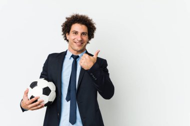 Futbol antrenörü elinde bir top tutuyor gülümsüyor ve başparmağını kaldırıyor.