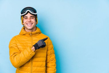 Snowboard gözlüğü takan genç kayakçı kendini soyutlamış, gülümseyen ve işaret eden boş alanda bir şey gösteriyor..