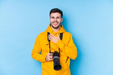 Kafkasyalı genç fotoğrafçı izole edilmiş kahkahalar atıyor ve elini göğsüne koyuyor..