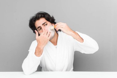 Gri bir arka planda sakalını kesen genç beyaz bir adam.