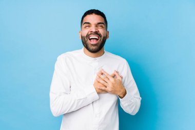 Mavi arka planda genç bir latin adam yalnız gülüyor, elini yüreğine koyuyor, mutluluk kavramını koruyor..