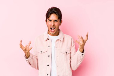 Pembe arka planda poz veren genç beyaz adam öfkeyle bağırıyor..