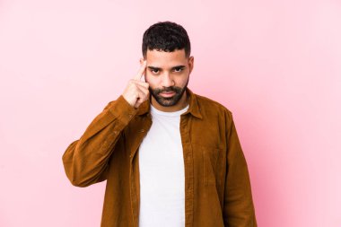 Pembe arka planı olan genç bir latin adam, tapınağı parmağıyla işaret ediyor, düşünüyor ve bir göreve odaklanıyor..