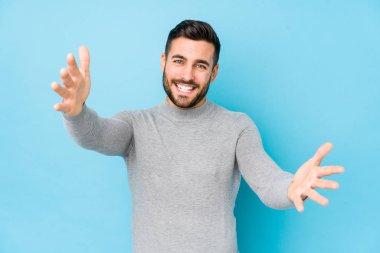 Mavi arka planda genç beyaz bir adam kendini kameraya sarılmış hissediyor..