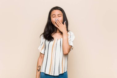 Genç, sevimli Çinli genç sarışın kadın pembe arka planda paltosunu giyiyor esniyor yorulmuş bir jestle ağzını eliyle kapatıyor..