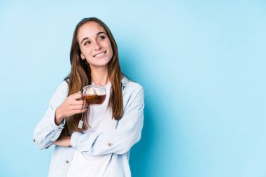 Elinde çay tutan beyaz bir kadın izole edilmiş, kollarını kavuşturarak gülümsüyor..