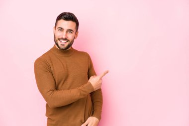 Pembe arka planda genç beyaz bir adam izole edilmiş gülümsüyor ve boş bir alanda bir şeyler gösteriyor..