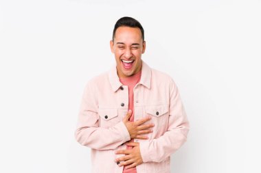 Yalnız poz veren genç Latin adam mutlu bir şekilde gülüyor ve ellerini karnının üstünde tutarak eğleniyor..