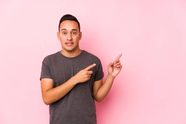 Yooung Latin adam pembe arka planda poz veriyor işaret parmaklarıyla fotokopi alanını işaret ediyor..