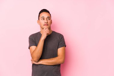 Pembe arka planda poz veren yog latin adam şüpheli ve şüpheci bir ifade takınıyor..