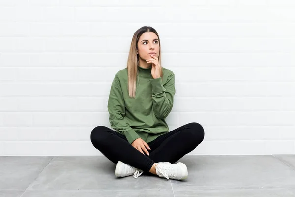 Jovem Caucasiana Sentada Chão Olhando Para Lados Com Expressão Duvidosa — Fotografia de Stock