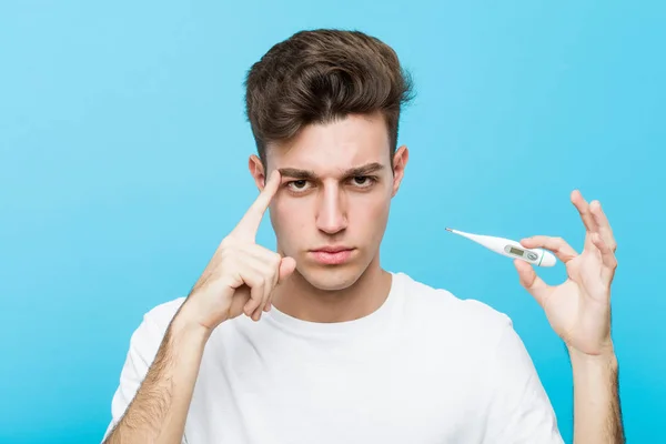 Young Caucasian Man Holding Medical Thermometer Pointing His Temple Finger — ストック写真