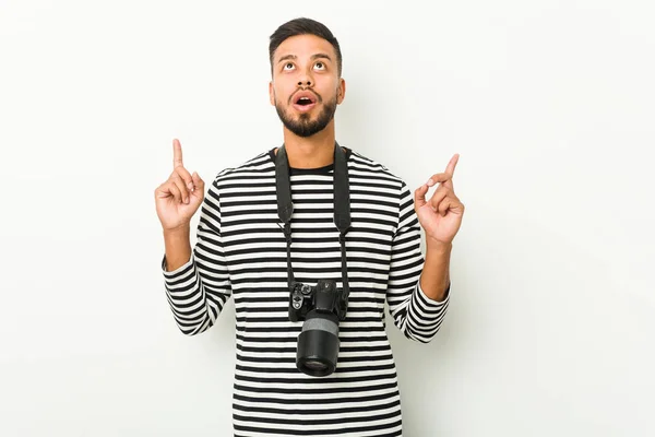 Young south-asian photographer pointing upside with opened mouth.