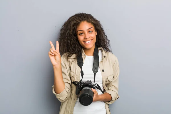 若いアフリカ系アメリカ人の写真家の女性は 指で2番目を示すカメラを持って — ストック写真
