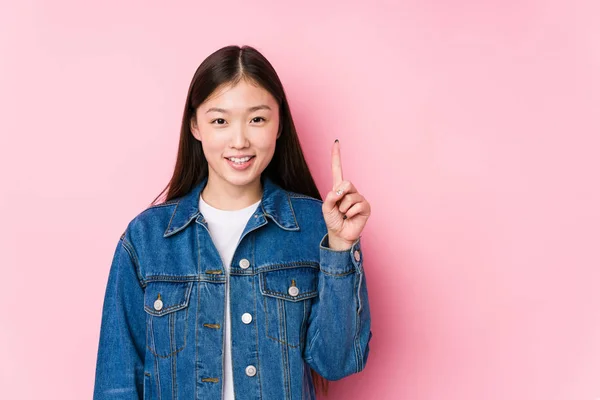 年轻的中国女人在粉色的背景上摆出一副无名小卒的样子 带着第一个手指 — 图库照片