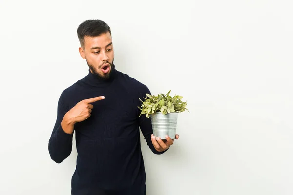 Joven Hombre Sudasiático Sosteniendo Una Planta Apuntando Hacia Lado — Foto de Stock