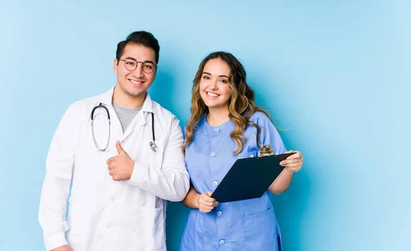 年轻的医生夫妇摆出一副蓝色的样子 面带微笑 竖起大拇指 — 图库照片