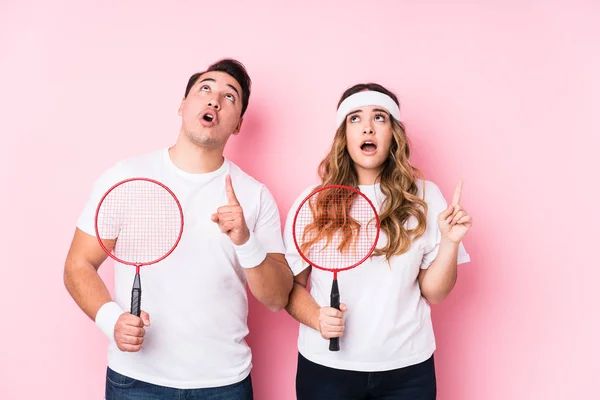 Casal Jovem Jogando Badminton Isolado Apontando Cabeça Com Boca Aberta — Fotografia de Stock