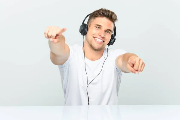 Mladý Muž Poslouchá Hudbu Sluchátky Veselé Úsměvy Ukazuje Dopředu — Stock fotografie