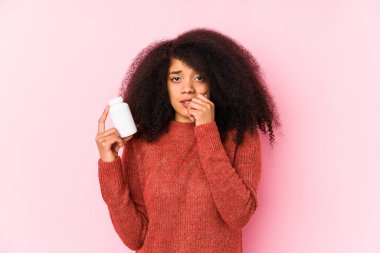 Vitaminlerini tutan genç afro bir kadın vitamin yiyen tırnakları tutan genç bir afro kadın, gergin ve endişeli..