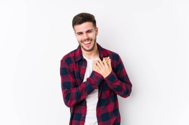 Beyaz arka planda poz veren beyaz tenli genç adam gülüyor, elini kalbe koyuyor, mutluluk kavramını koruyor..