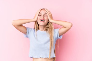 Pembe arka plandaki genç sarışın kadın ellerini başının üstünde tutarak neşe içinde gülüyor. Mutluluk kavramı.
