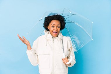 Şemsiyesini tutan genç Afrikalı Amerikalı kadın hoş bir sürprizle karşılaşıyor, heyecanlı ve el kaldırıyor..