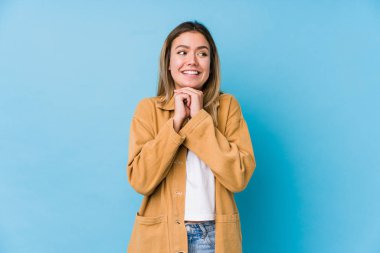 Genç beyaz kadın ellerini çenesinin altında tutuyor, mutlu bir şekilde yan tarafa bakıyor..