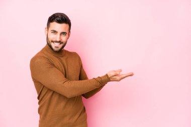 Pembe arka planı olan genç beyaz bir adam bir palmiye üzerinde bir kopya alanı tutuyor..