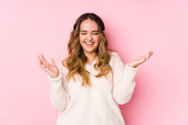 Pembe arka planda poz veren kıvrımlı genç bir kadın neşeli bir şekilde gülüyor. Mutluluk kavramı.