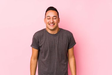 Pembe arka planda poz veren yog latin adam gülüyor ve gözlerini kapatıyor, rahatlamış ve mutlu hissediyor..
