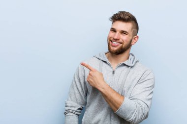 Genç yakışıklı fitness adamı gülümsüyor ve boş alanda bir şeyler gösteriyor..