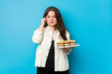 Genç, kıvrımlı bir kadın elinde keklerle tapınağı işaret ediyor. Düşünüyor, bir işe odaklanıyor..