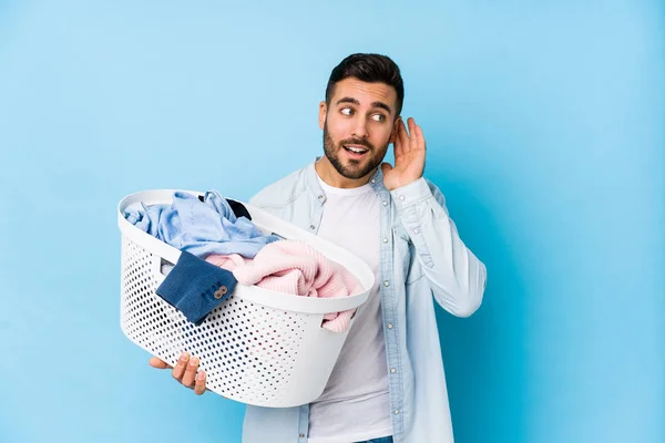 Young handsome man doing laundry isolated trying to listening a gossip.