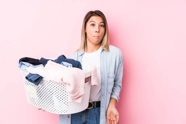 Young Caucasian Woman Picking Dirty Clothes Shrugs Shoulders Open Eyes — Stock Photo, Image