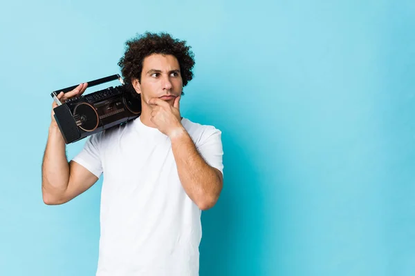 Young Caucasian Curly Man Holding Guetto Blaster Looking Sideways Doubtful — 스톡 사진