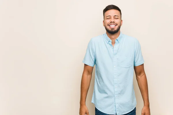 Young south-asian man laughs and closes eyes, feels relaxed and happy.