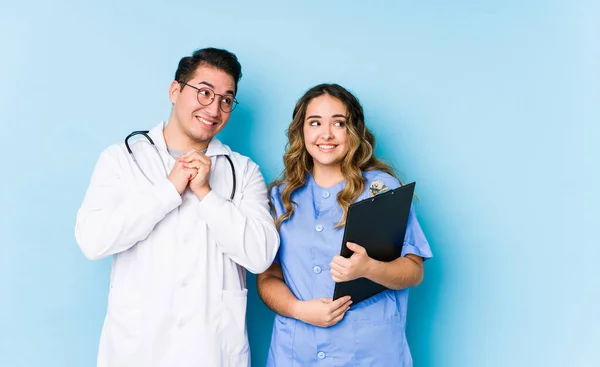 Young Doctor Couple Posing Blue Background Isolated Keeps Hands Chin — 스톡 사진