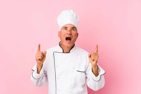 Middle aged cook man isolated pointing upside with opened mouth.