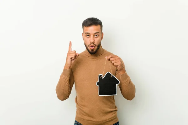 Young south-asian man holding a home icon having some great idea, concept of creativity.