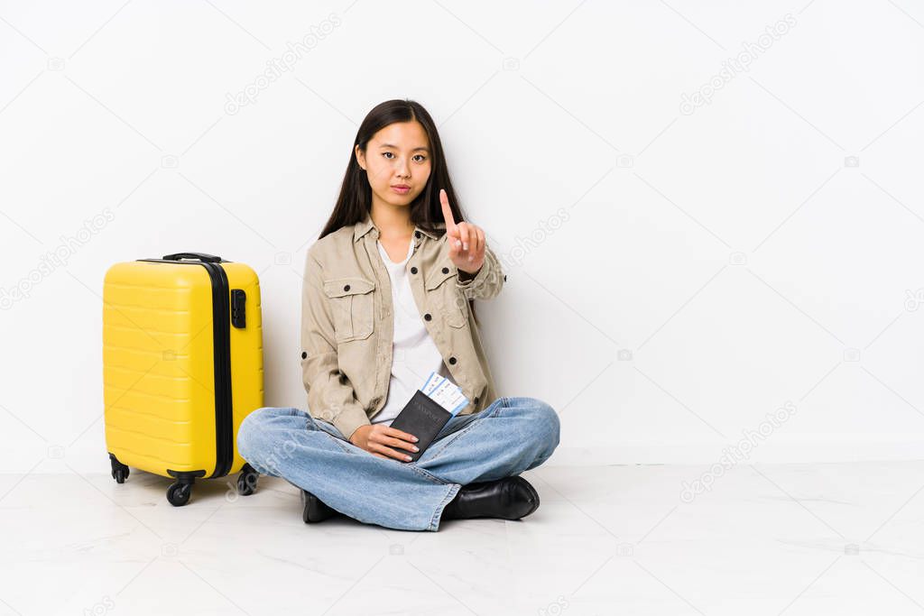 Young chinese traveler woman sitting holding a boarding passes showing number one with finger.